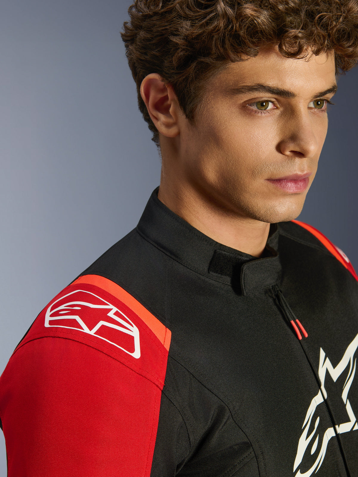 Casaco Alpinestars T-SPS V2 Waterproof, casaco têxtil de motociclismo, preto, vermelho e vermelho fluo, grande plano de modelo a usar o casaco, com logótipos brancos proeminentes da Alpinestars no ombro e no peito, gola de perfil baixo e corte desportivo.