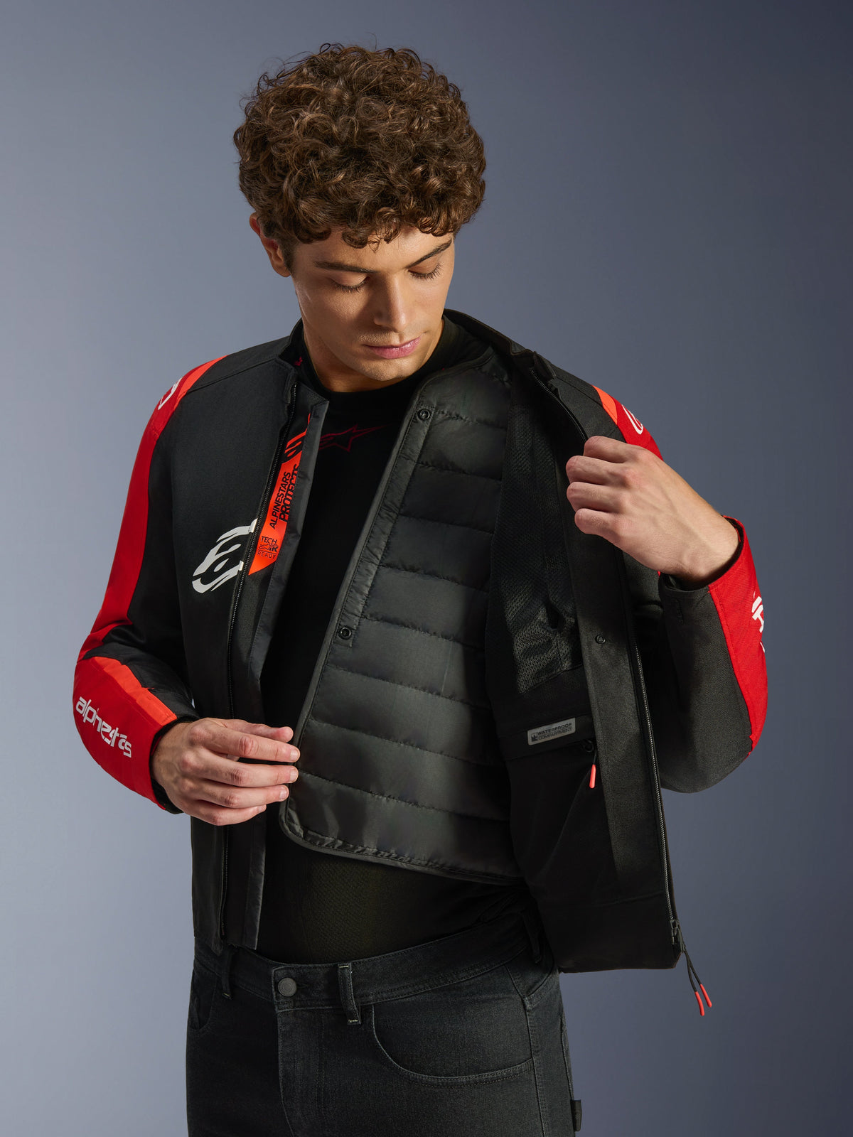 Casaco Alpinestars T-SPS V2 Waterproof, preto e vermelho, com modelo a revelar o forro térmico acolchoado interno e o compartimento impermeável, marcação Tech-Air Ready no interior, casaco de motociclismo com corte desportivo.