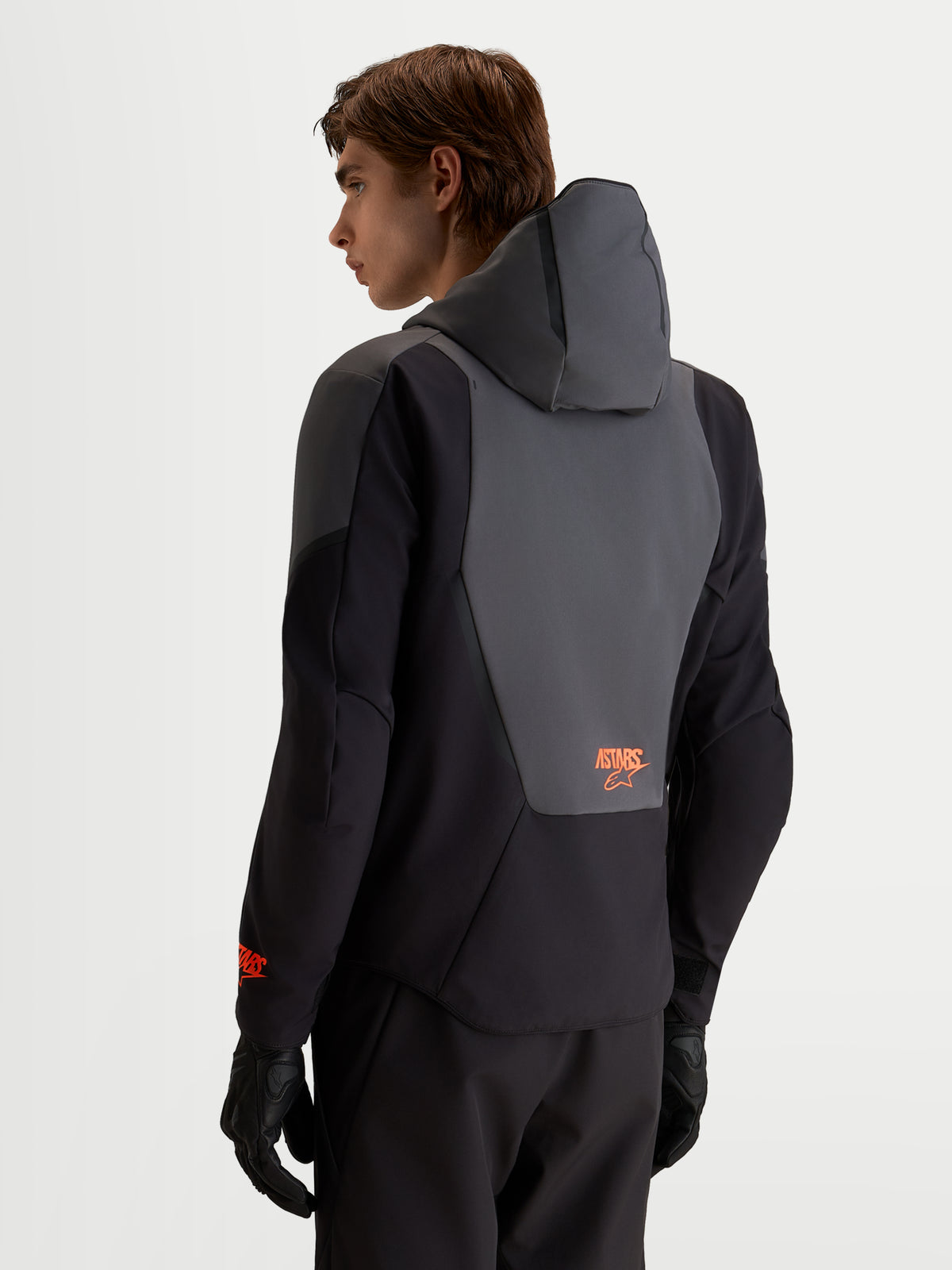 Alpinestars Aeroshell Waterproof Jacket, blusão de moto softshell para homem, preto e cinzento escuro, vista traseira num modelo com capuz integrado e detalhe no painel traseiro