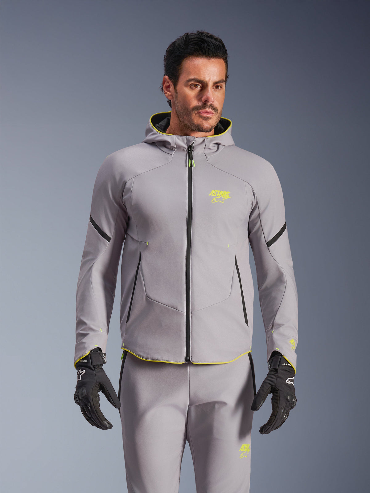 Alpinestars Aeroshell Waterproof Jacket, casaco softshell de motociclismo com capuz, cinzento médio e amarelo fluorescente com fechos de correr pretos, usado com calças cinzentas a condizer e luvas pretas, equipamento impermeável de alta performance para estrada