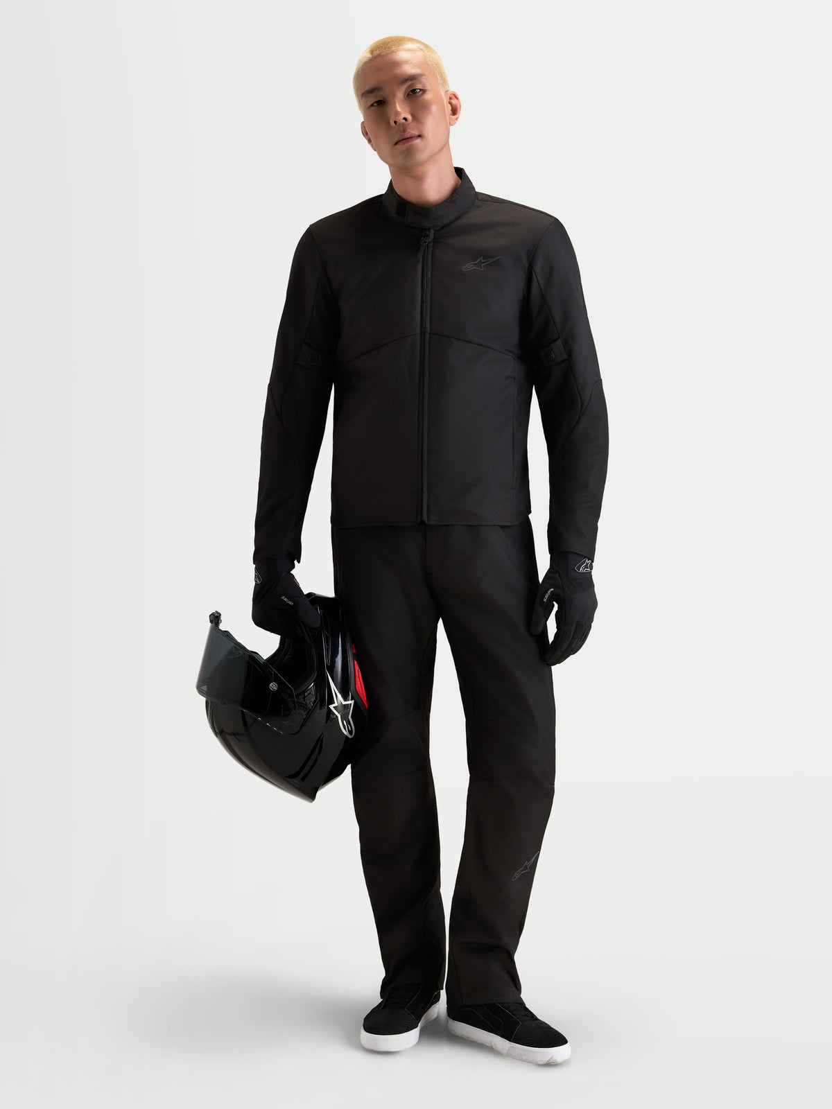 Alpinestars C-1 Waterproof, blusão de moto urbano contemporâneo para homem, preto, vista frontal num modelo com calças a condizer, a segurar um capacete e a usar luvas de moto