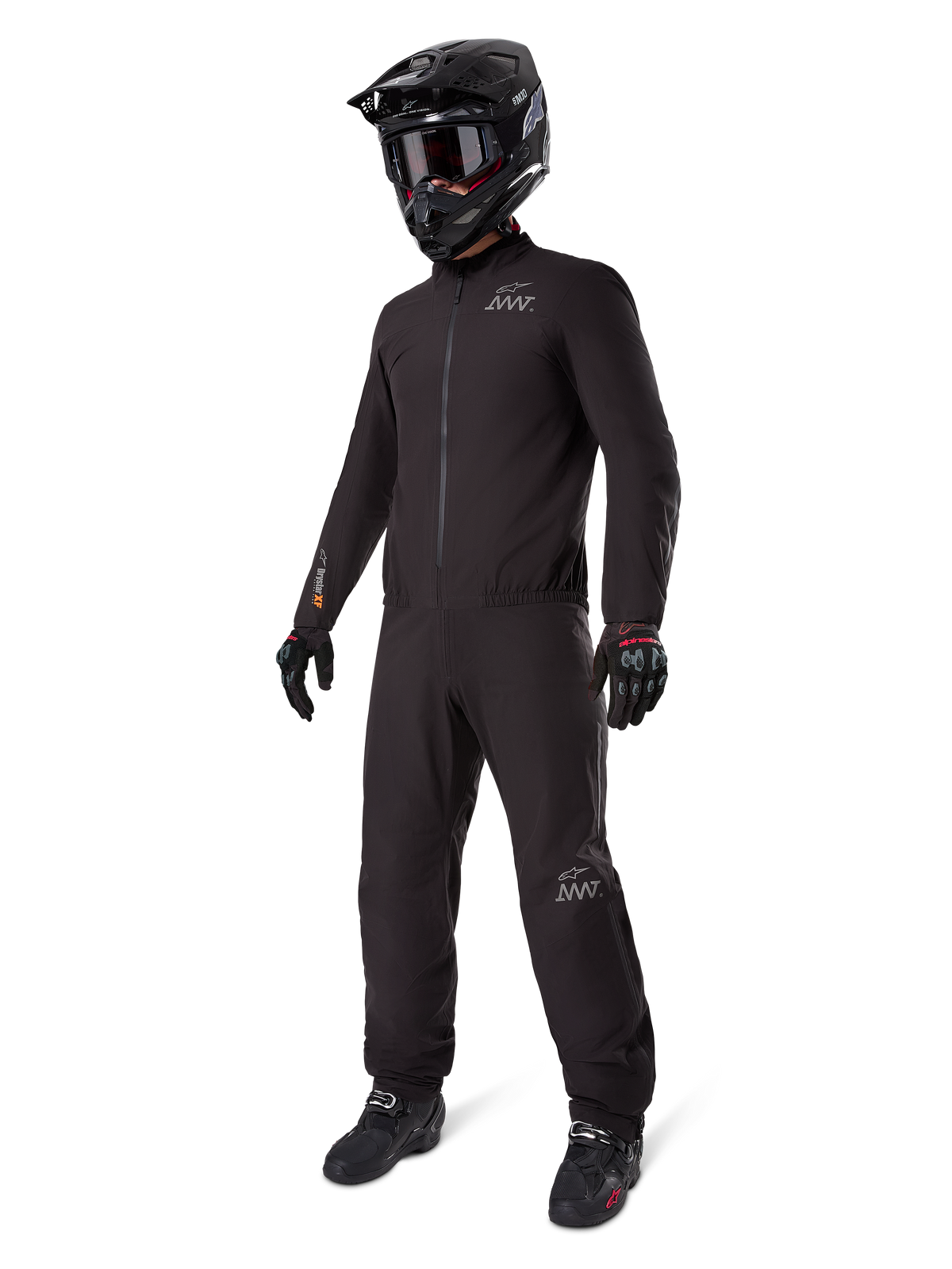 Alpinestars AMT-8 Stretch Drystar® XF Liner, fato de motociclismo impermeável preto, usado com capacete preto, óculos e luvas, com logótipos AMT e Drystar XF, equipamento de aventura funcional para proteção em todas as condições climatéricas.