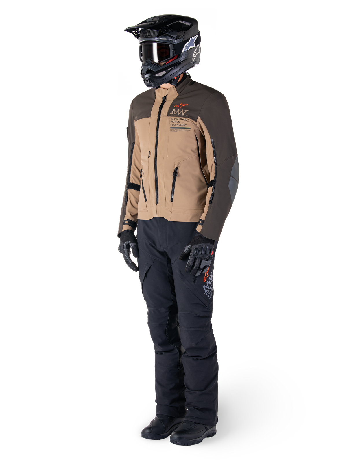 Motociclista de aventura com equipamento completo, casaco Alpinestars AMT-8 Stretch Drystar® XF em castanho escuro e khaki escuro, combinado com calças de aventura pretas, capacete preto, luvas e botas, com logótipo AMT em laranja e fechos de ventilação técnicos para viagens de longa distância