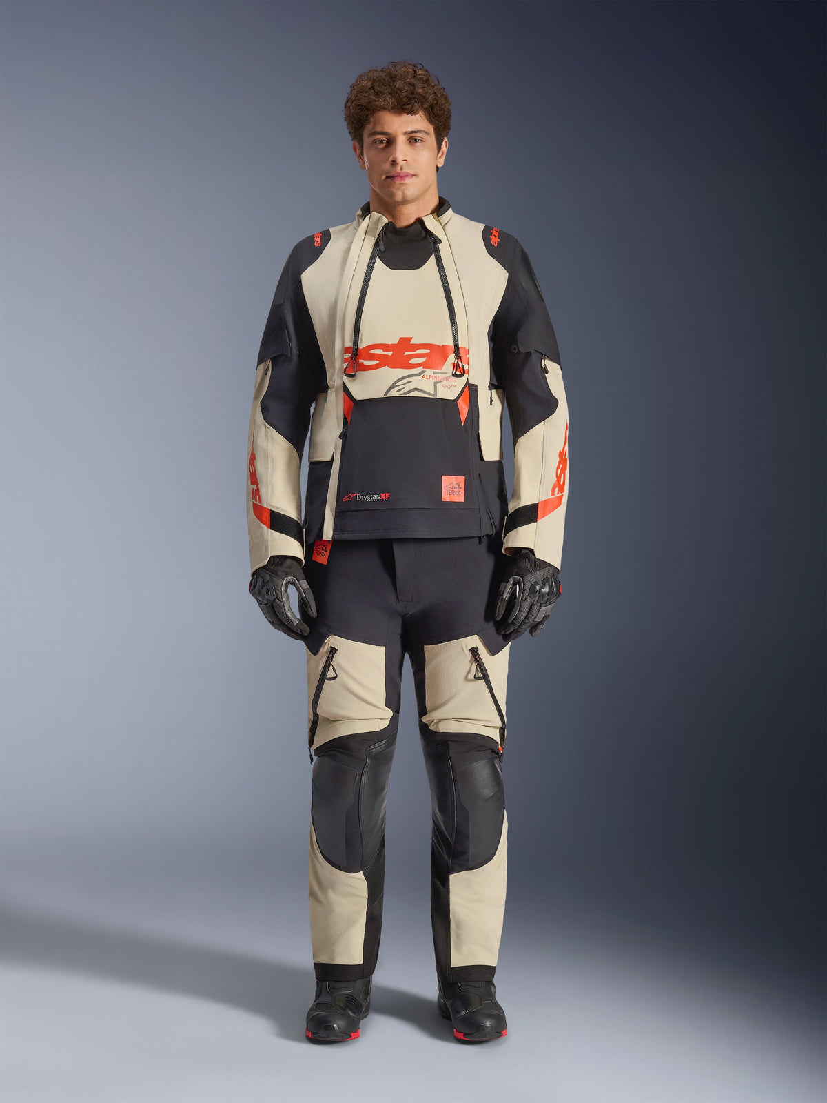 Casaco Alpinestars Halo Pro Drystar® XF Laminated, Mastic Black, casaco de aventura para motociclismo usado por um modelo com calças e luvas a condizer, painéis têxteis bege e pretos com logótipos vermelhos em destaque, design modular para condução em todo-o-terreno