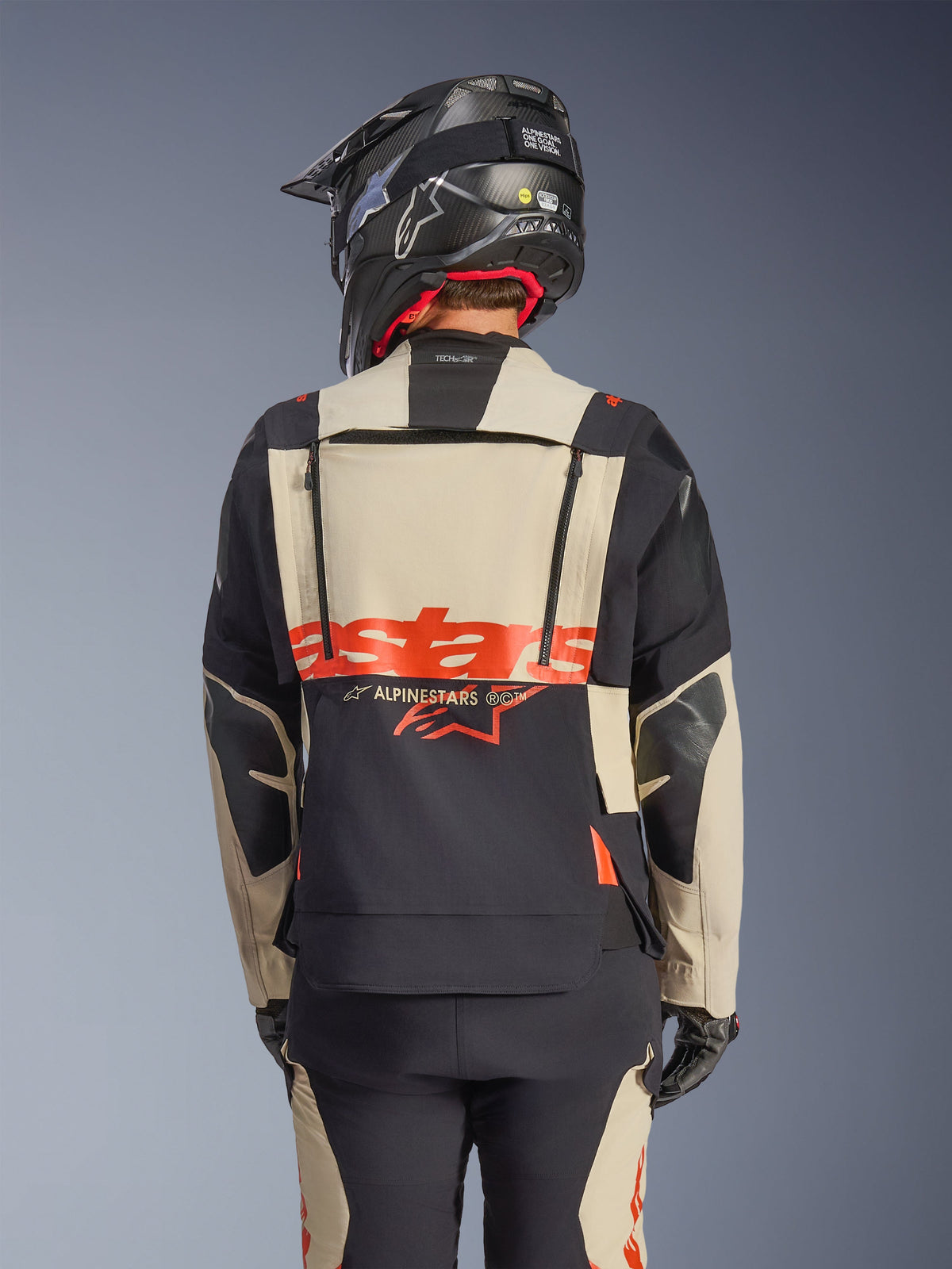 Casaco Alpinestars Halo Pro Drystar® XF Laminated em Mastic Black, vista traseira mostrando o painel traseiro modular com logótipo vermelho e fechos de ventilação, usado por um motociclista com calças de aventura a condizer e capacete preto