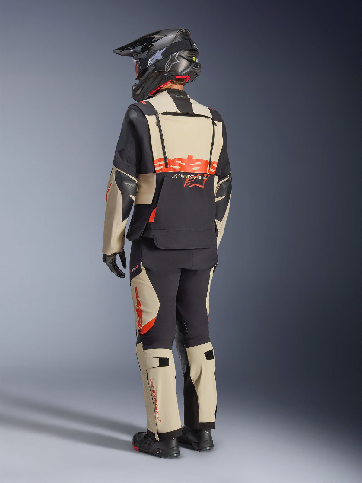 Casaco Alpinestars Halo Pro Drystar® XF Laminado, Mastic Black, vista traseira de um motociclista a usar o fato de aventura completo com calças a condizer, capacete de aventura preto e botas, com um logótipo Alpinestars vermelho em destaque nas costas.