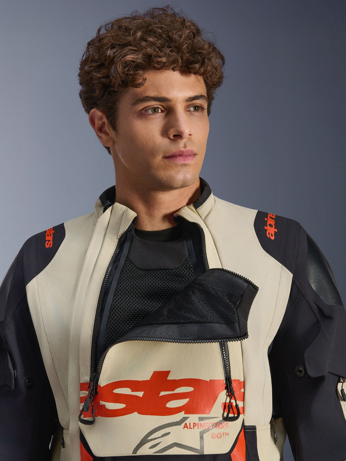 Alpinestars Halo Pro Drystar® XF Laminated Jacket em Mastic Black, modelo masculino a usar o casaco com o painel de ventilação frontal do peito aberto para mostrar a camada interior em malha, com logótipos a vermelho e painéis pretos nos ombros, equipamento técnico de motociclismo de aventura