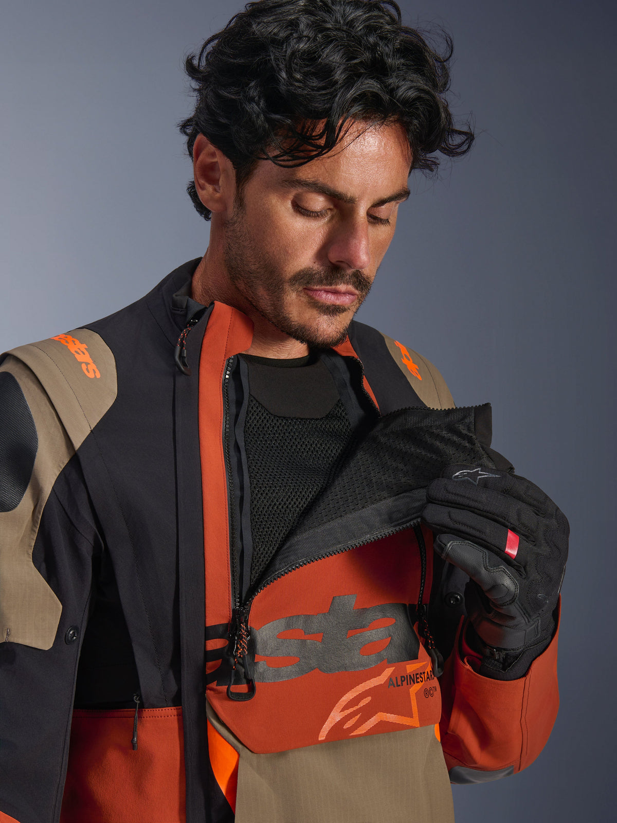 Alpinestars Halo Pro Drystar® XF Laminated Jacket, Walnut Rust Black colorway, male model demonstrating modular ventilation system by unzipping the front chest panel to reveal black mesh, technical adventure motorcycle jacket with rust and tan accents.
