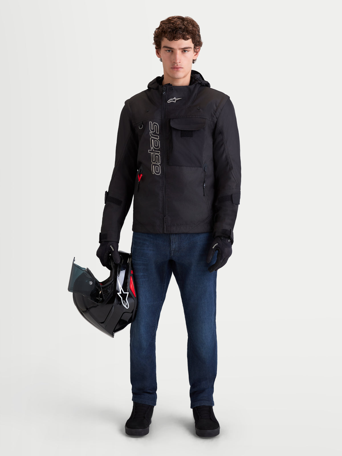 Alpinestars Morfex Parka Wp Jkt, casaco de moto para homem, preto, vista frontal num modelo a usar calças de ganga e a segurar um capacete, destacando o design modular e o capuz integrado