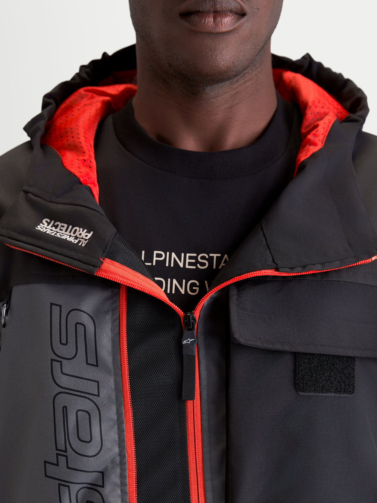 Alpinestars Morfex Parka, casaco de moto impermeável para homem, cinzento e preto, vista de pormenor a mostrar o capuz integrado, o forro interior vermelho e os detalhes do bolso no peito num modelo
