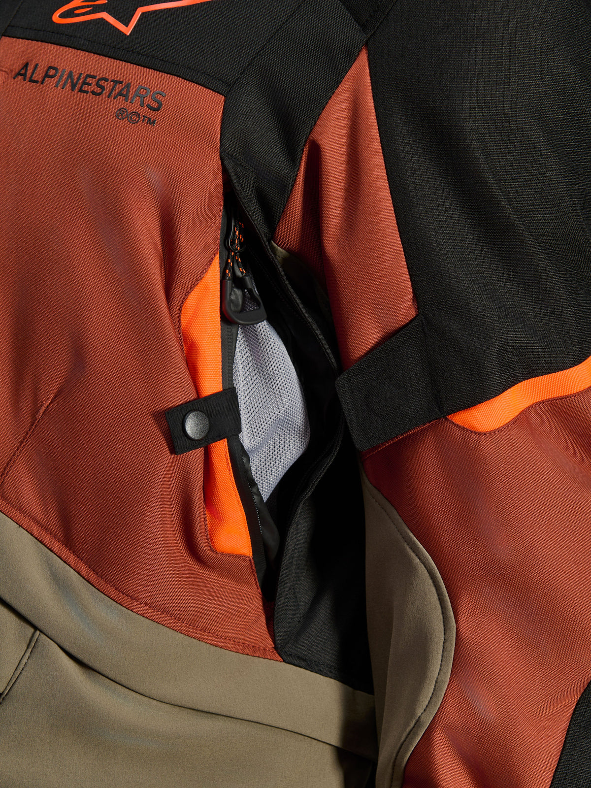 Alpinestars Andes V4 Drystar® Jacket, Walnut Rust Black, close-up of direct ventilation vent with mesh lining, durable textile material with orange accents, snap button and Alpinestars logo detail