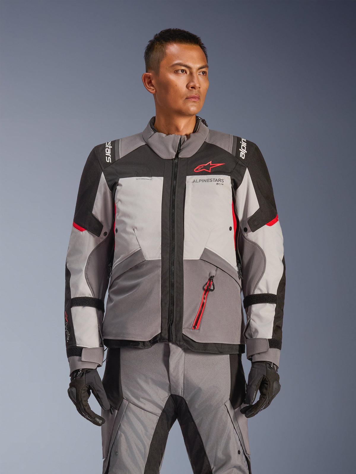 Casaco Alpinestars Andes V4 Drystar®, casaco de motociclismo para turismo de aventura, cinzento escuro e cinzento gelo com detalhes em preto e vermelho vivo, usado com calças e luvas a condizer, design impermeável e respirável para condução de aventura em qualquer clima