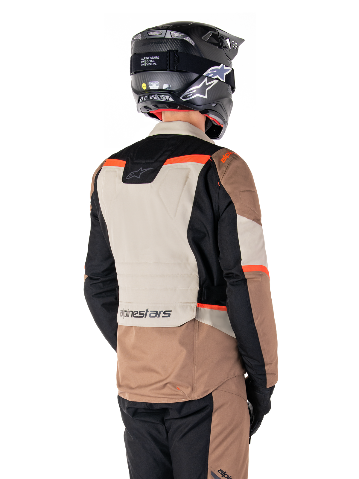 Casaco Impermeável Alpinestars ST-1, casaco de turismo de aventura, cáqui escuro, areia, preto e vermelho fluorescente, vista traseira com painéis têxteis em blocos de cor, detalhes em vermelho fluo e marca Alpinestars na zona inferior das costas, usado por um motociclista com capacete preto