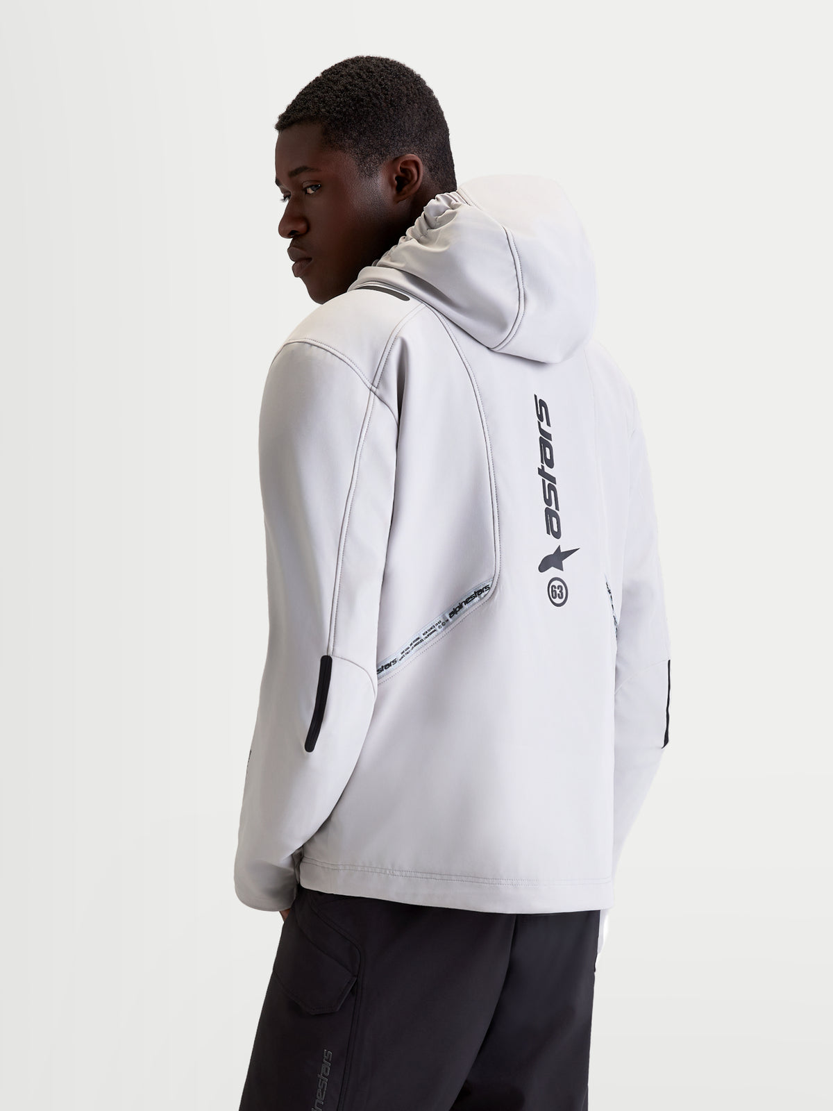 Alpinestars C 5 Drystar casaco de moto urbano para homem, cinzento e preto, vista traseira num modelo a mostrar capuz integrado, construção em softshell e detalhes com logótipo vertical nas costas