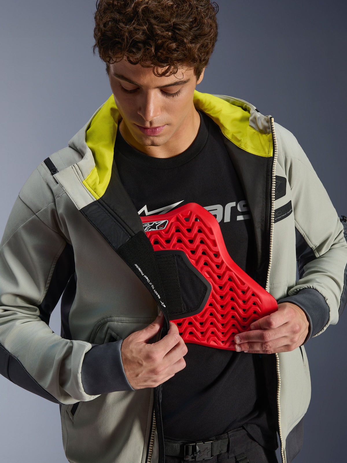 Alpinestars Moblast Waterproof Jacket, Iron Gray and Dark Sage, model demonstrating chest armor integration with a red protector insert, bright lime green interior lining, modern urban motorcycle riding gear