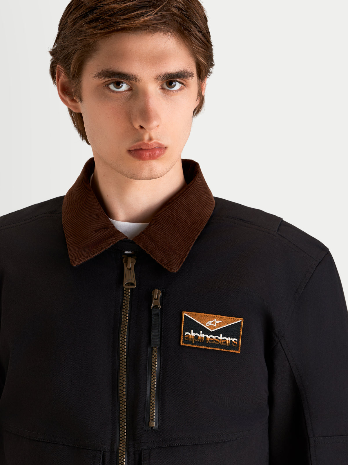 Alpinestars Mustang Waterproof Jacket, men's urban contemporary motorcycle textile jacket in dark anthracite and dark brown, close-up shot showing the workwear-inspired corduroy collar, front zip, and branded chest patch worn by a model.
