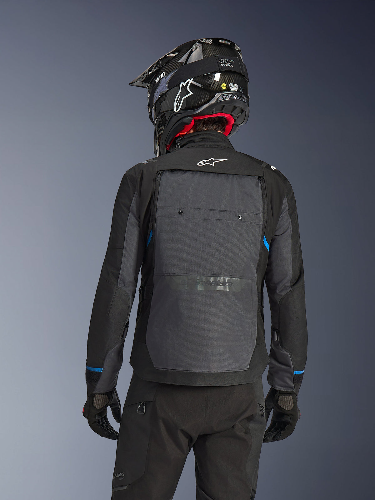 Piloto visto de costas a usar o Casaco Alpinestars Cusco Drystar® em preto e cinzento escuro, com um grande painel de ventilação cinzento nas costas e logótipo branco, combinado com um capacete de off-road preto e equipamento de condução preto para touring de aventura.