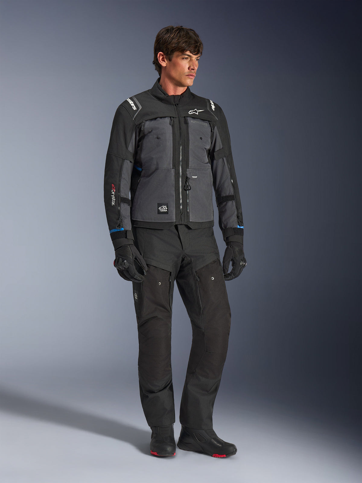 Casaco Alpinestars Cusco Drystar® em Preto e Cinzento Escuro, casaco técnico de motociclismo com painéis multi-tonais, usado com calças e luvas pretas a condizer, concebido para estrada e turismo de aventura.