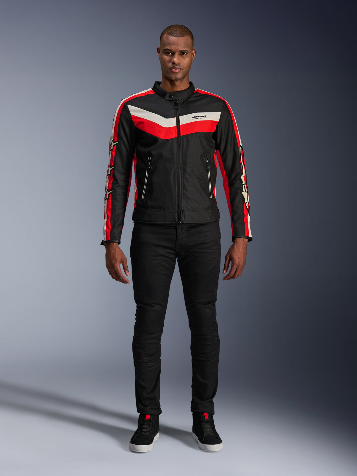 Casaco Alpinestars T-Dyno WR, casaco de motociclismo têxtil em preto, vermelho vivo e ecru, com riscas no peito em forma de V e logótipos de estrela nas mangas, usado com calças pretas e sapatos de condução pretos, equipamento urbano de inspiração clássica