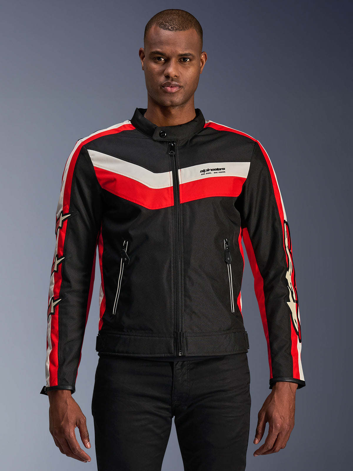 Alpinestars T-Dyno WR Jacket, casaco têxtil de motociclismo, preto com riscas em chevron vermelho vivo e cru, ajuste de motociclista de inspiração vintage, gola alta com fecho de botão, bolsos frontais com fecho de correr, logótipos de estrela nas mangas, vestido por um modelo