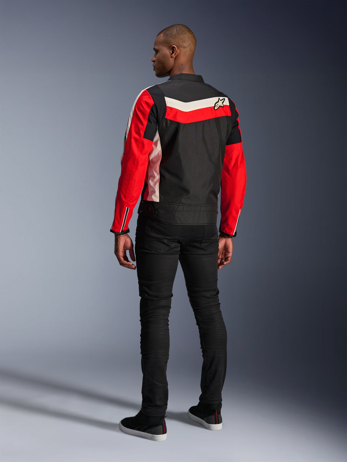 Alpinestars T-Dyno WR Jacket, casaco de motociclismo têxtil, preto, vermelho vivo e ecru, vista traseira num modelo, ajuste de motociclista de inspiração vintage com painéis de cores heritage e logótipo, equipamento de estrada urbano moderno