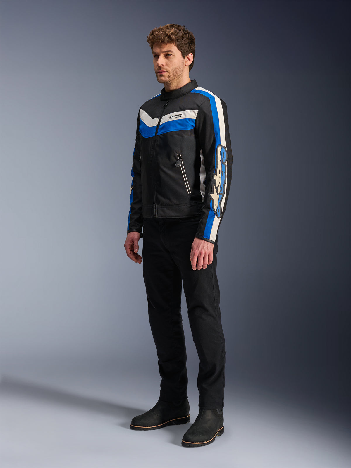 Casaco Alpinestars T-Dyno WR, preto, azul e cru, casaco de motociclismo têxtil usado por um modelo com calças e botas pretas, design de inspiração vintage com riscas arrojadas em azul e cru e logótipos nas mangas, fotografia de estúdio