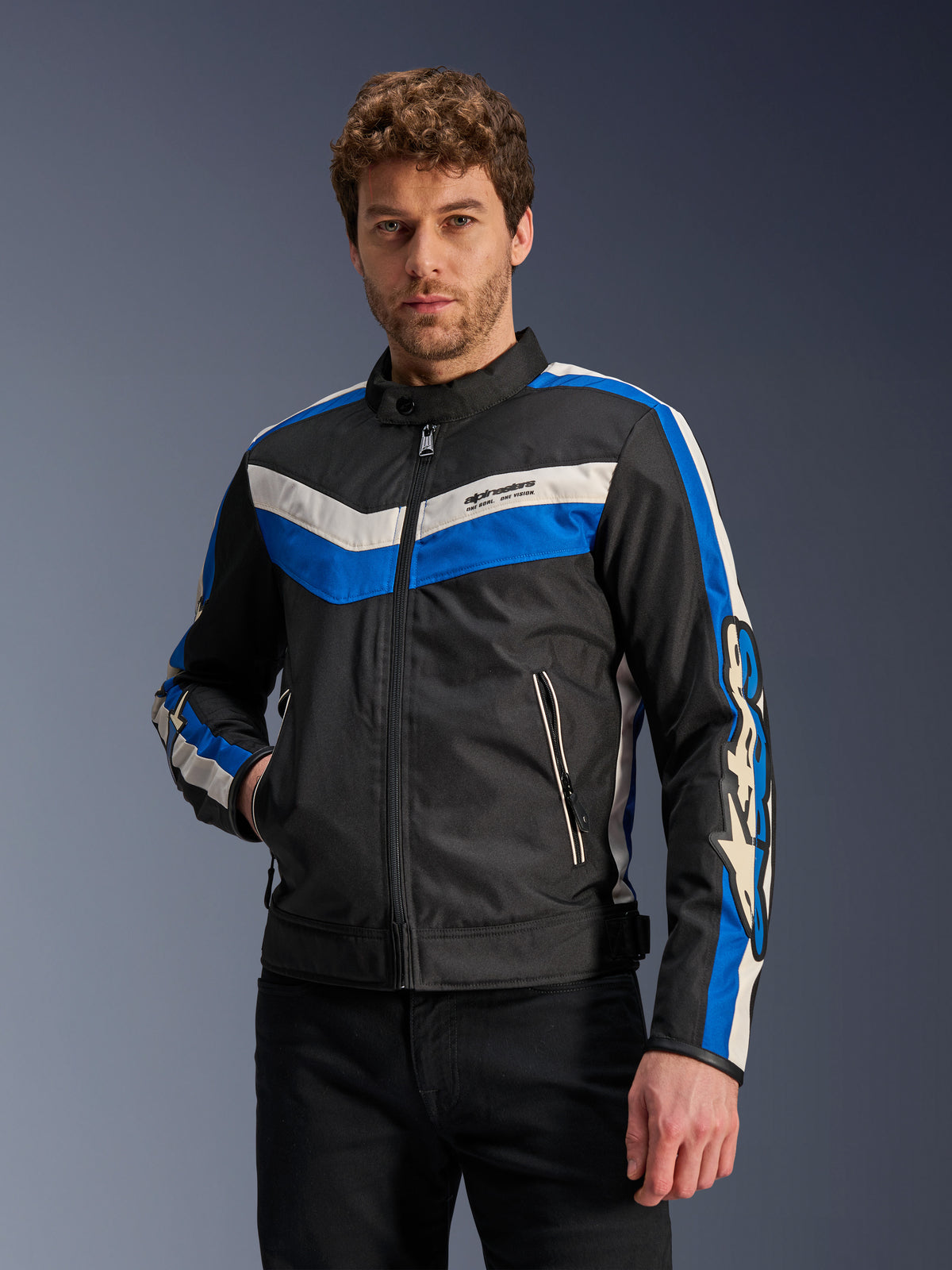 Casaco Alpinestars T-Dyno WR em Preto Azul Ecru, casaco têxtil de motociclismo com riscas chevron azuis e off-white no peito e nas mangas, vestido por um modelo