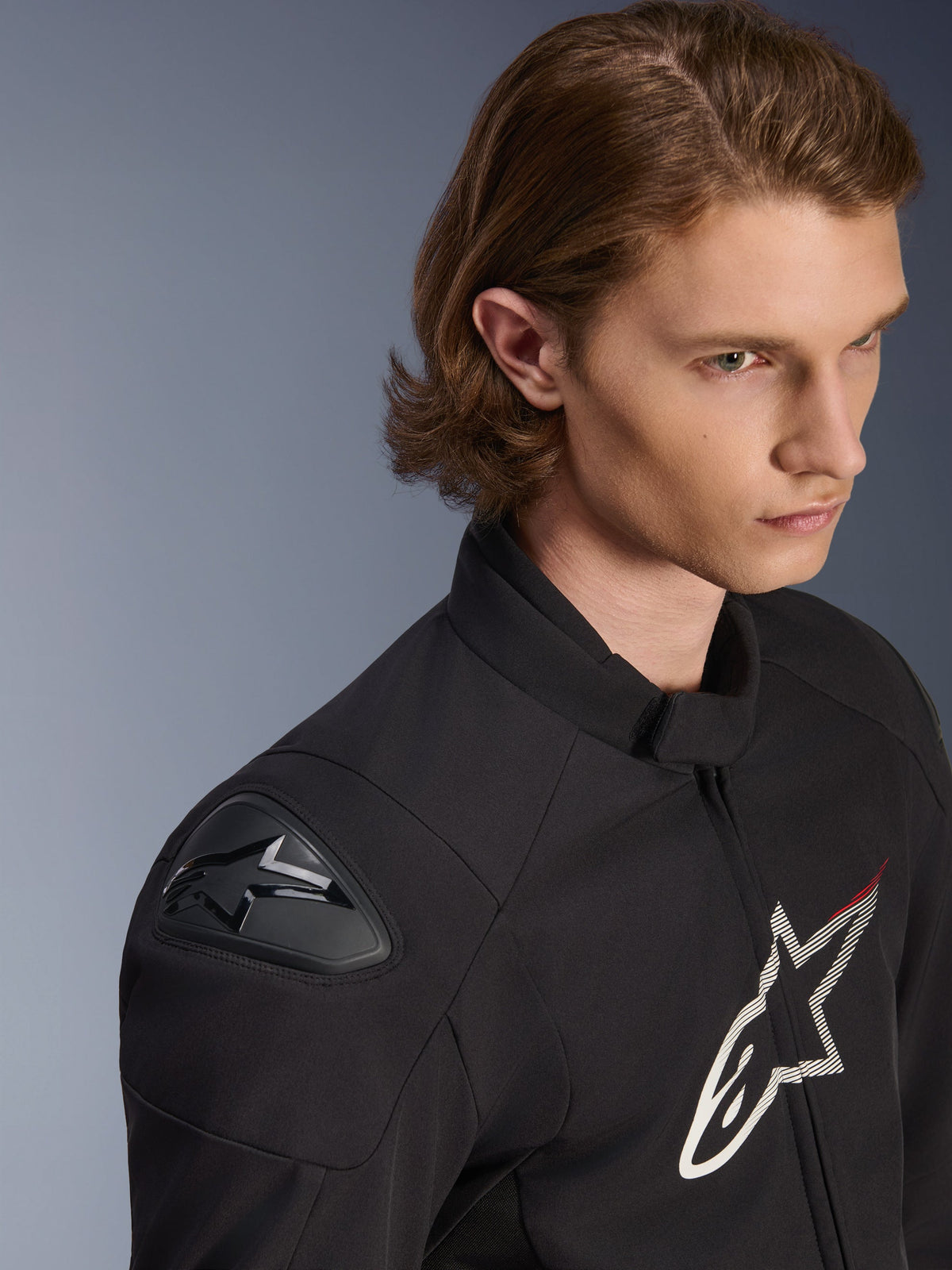 Alpinestars SMX Waterproof Jacket, casaco impermeável preto com detalhes em branco e vermelho, plano aproximado num modelo masculino, com protetores de ombro externos DFS Lite e logótipo de estrela grande no peito, vestuário desportivo para motociclismo