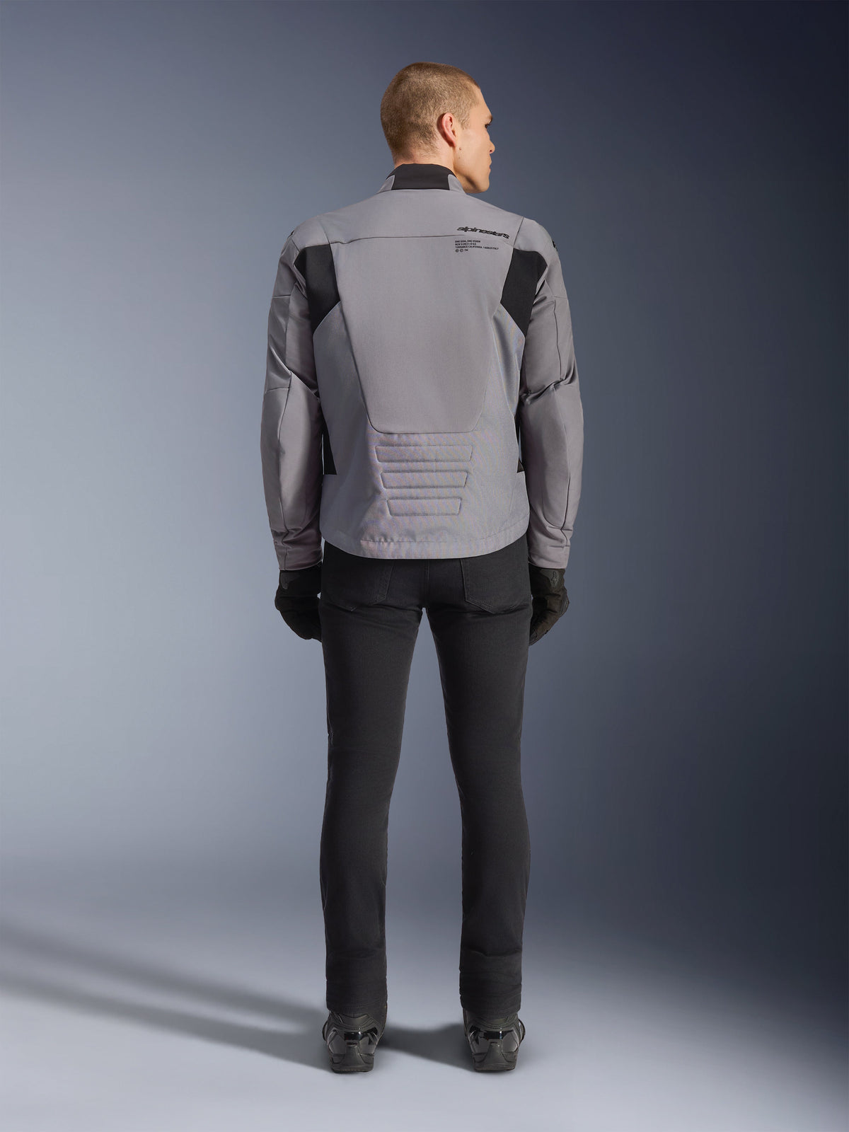 Casaco Alpinestars SMX Waterproof, vista traseira, cinzento escuro e preto, com painéis têxteis pretos nos ombros e design de ajuste desportivo, combinado com calças e luvas pretas para um visual completo de motociclismo