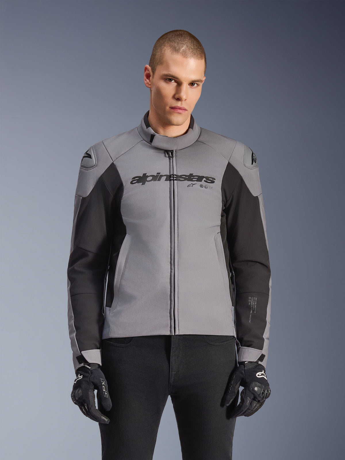 Casaco Alpinestars SMX Waterproof, casaco de motociclismo de estrada desportivo, cinzento escuro e preto, com gola alta e sliders de ombro DFS Lite, usado com luvas SMX pretas, corte atlético elegante para condução em todas as condições climatéricas