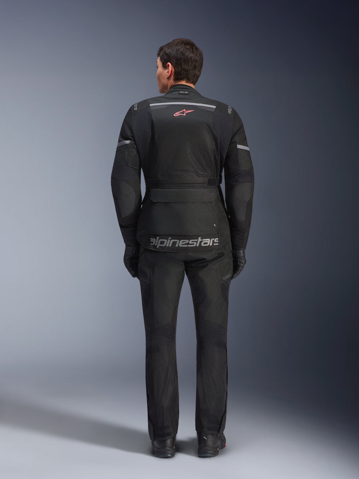 Vista traseira de um motociclista com o Casaco Alpinestars Andes Air Drystar® em preto, com extensos painéis de ventilação em malha nas costas, logótipo Alpinestars vermelho e detalhes refletores, em conjunto com calças e luvas de motociclismo para touring de aventura
