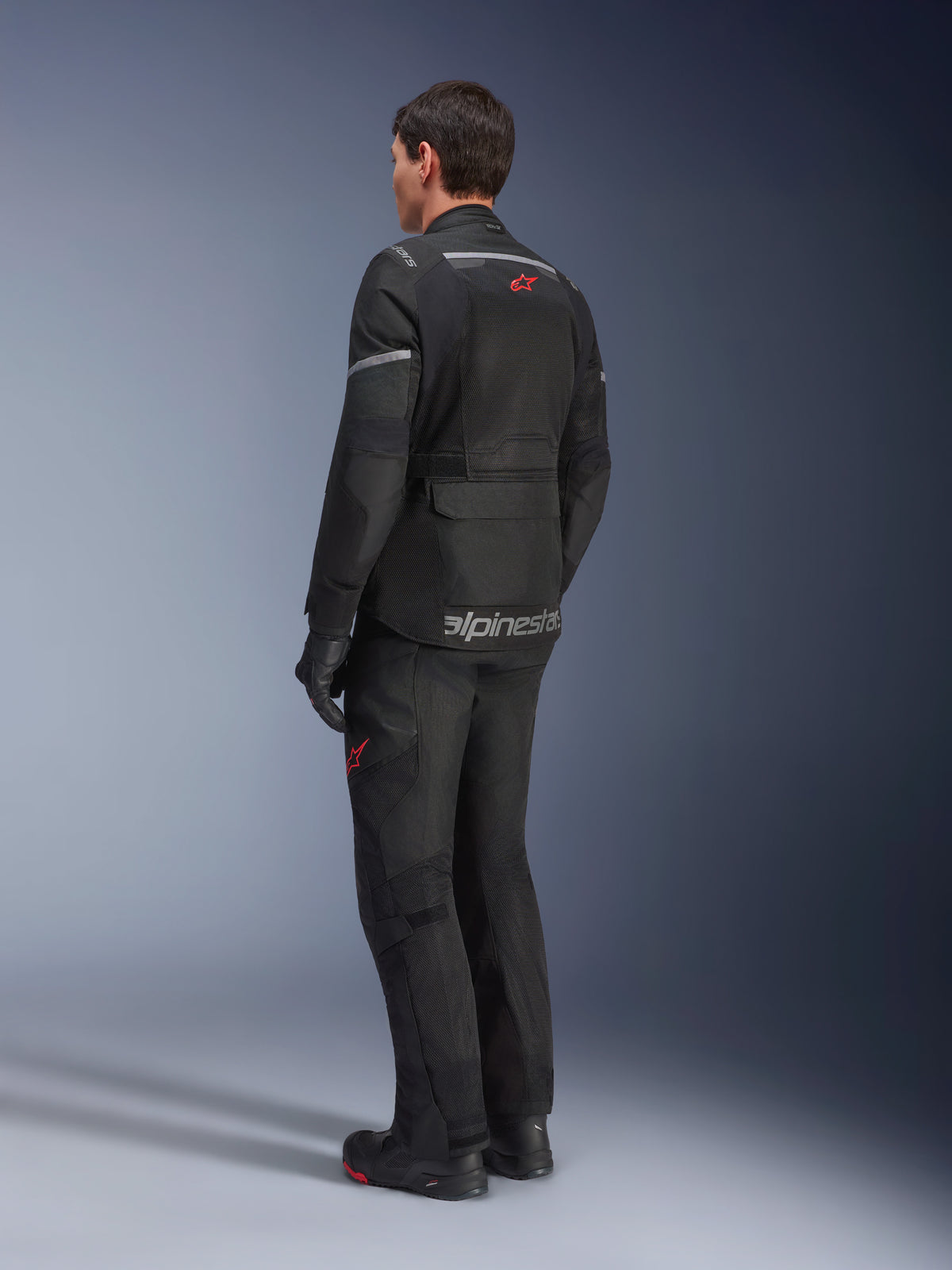 Casaco Alpinestars Andes Air Drystar®, preto, vista traseira num motociclista, com painéis de malha extensos para ventilação, usado com calças e botas de motociclismo de aventura a condizer, demonstrando o design de touring e a imagem da marca.
