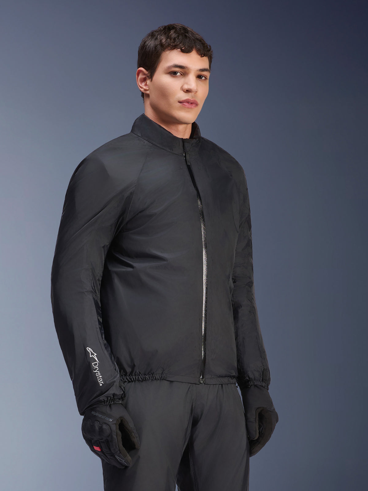 Membrana impermeável do Casaco Alpinestars Andes Air Drystar®, preta, usada por um modelo masculino com luvas e calças pretas, têxtil técnico leve com a marca 'Drystar' na manga, fotografia de estúdio