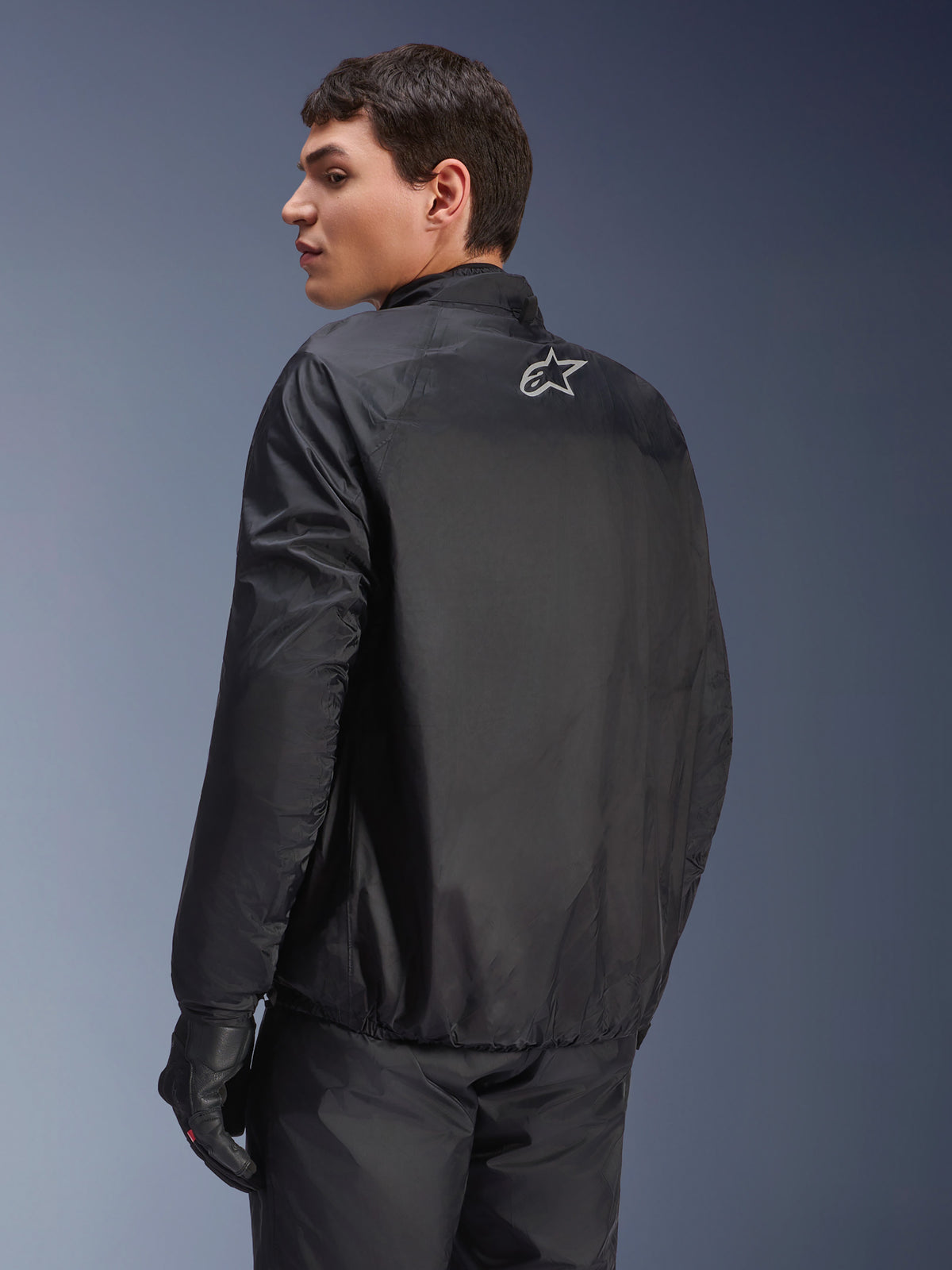Casaco Alpinestars Andes Air Drystar®, membrana impermeável destacável em preto, vista traseira num modelo masculino, com um pequeno logótipo Alpinestars branco na parte superior das costas, combinado com luvas de motociclismo pretas