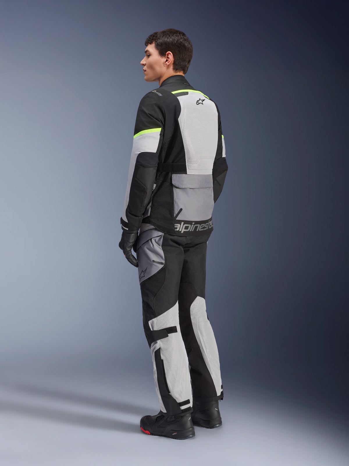 Rider wearing Alpinestars Andes Air Drystar® Jacket and Pants, adventure touring gear in Ice Gray Dark Gray Black with neon yellow accents, featuring extensive mesh panels for airflow, Alpinestars branding on the back, worn with black gloves and boots.