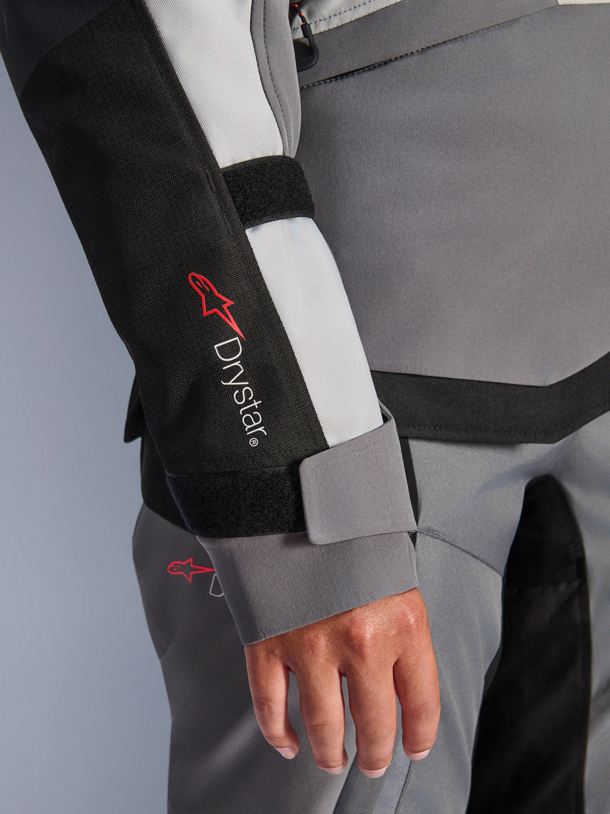 Alpinestars Stella Andes V4 Drystar®, casaco de aventura feminino cinzento, pormenor da manga com logótipo e fecho de velcro.