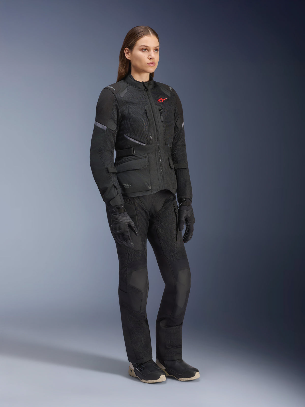 Mulher a usar o Casaco Alpinestars Stella Andes Air Drystar®, casaco têxtil de aventura e touring em preto, combinado com calças e luvas pretas a condizer, com grandes painéis de ventilação em malha e logótipo vermelho, conjunto coordenado de motociclismo para mulher