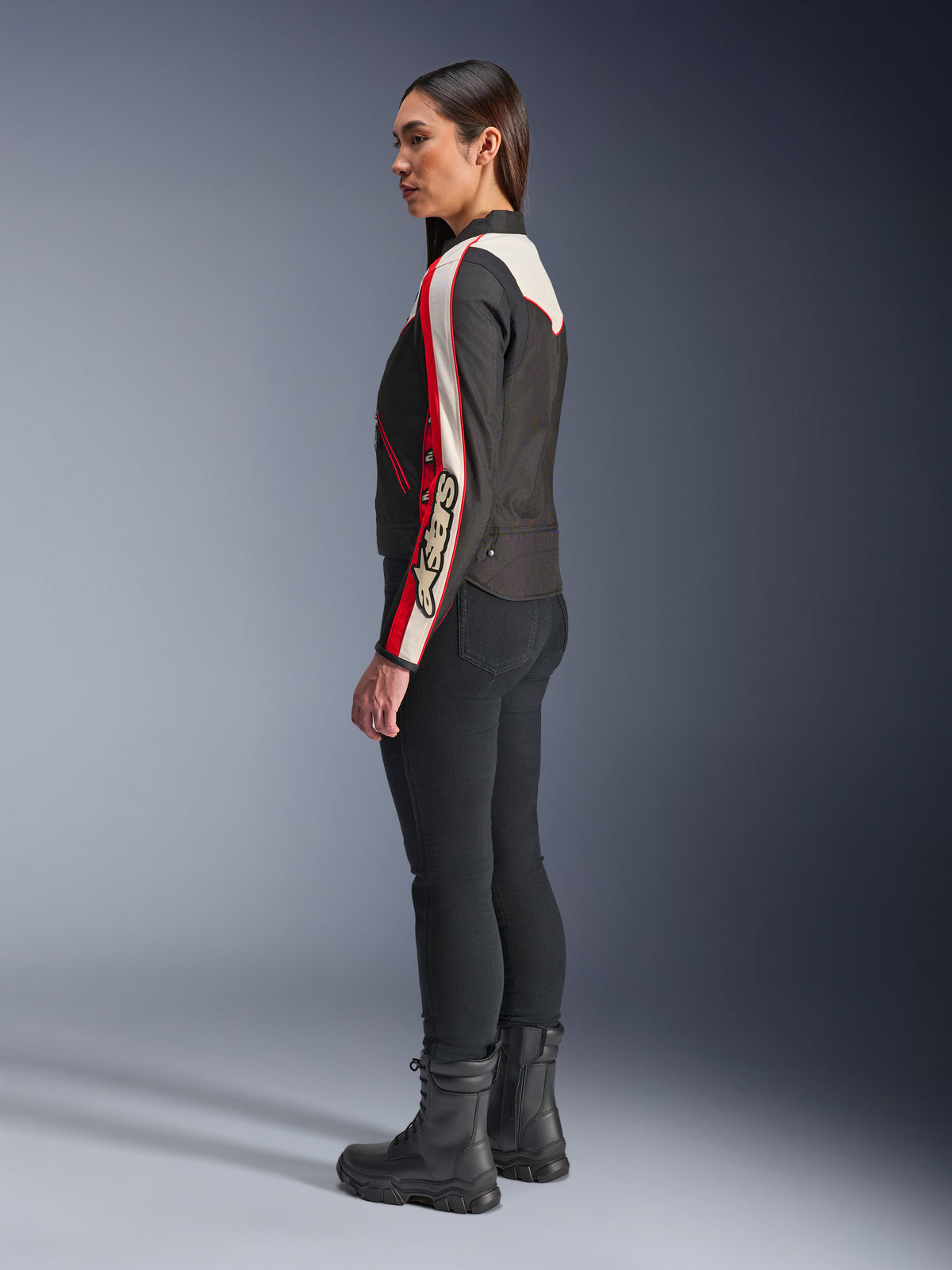 Casaco Alpinestars Stella T-Dyno WR, casaco de motociclismo têxtil para mulher, preto, cru e vermelho vivo, com design de inspiração vintage e marca Astars na manga, usado com calças pretas justas e botas pretas, corte de motociclista mais curto para condução urbana.