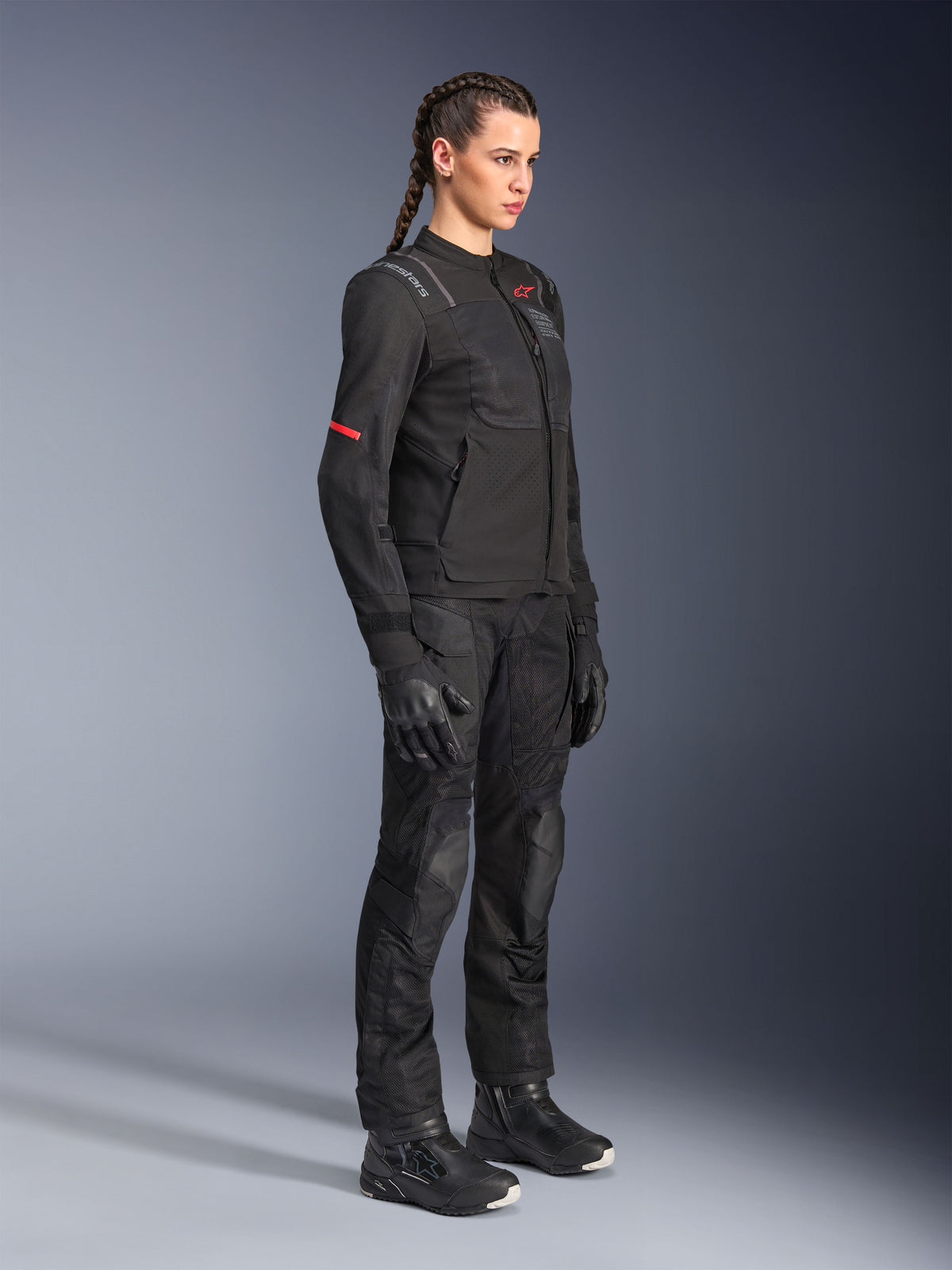 Female model wearing the Alpinestars Stella ST-2 Air Jacket in Black, paired with matching black motorcycle pants, gloves, and boots, featuring mesh ventilation panels and subtle red details, sleek modern touring outfit