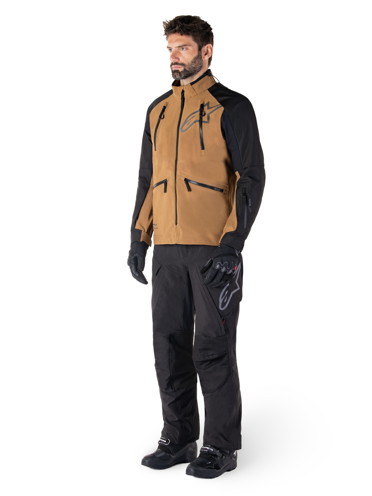 Calças Alpinestars Hyde XT Drystar®, calças de motociclismo de aventura, pretas, usadas com um casaco técnico castanho e preto, luvas e botas pretas, com um design por cima da bota para condução off-road e dual-sport