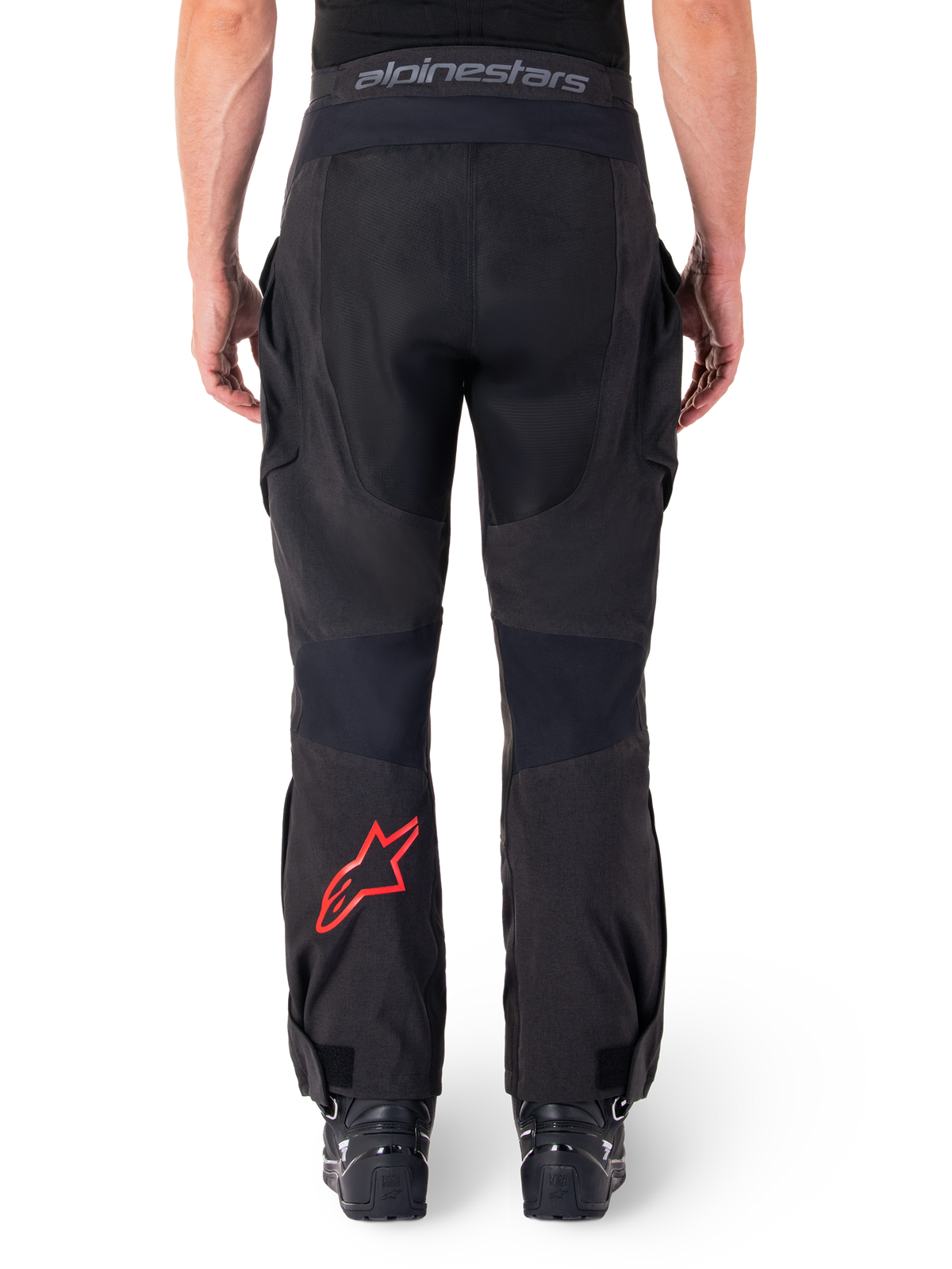 Calças Alpinestars Hyde XT Drystar®, calças de motociclismo de aventura, pretas com logótipo de estrela vermelho na parte inferior da perna, vista traseira, design enduro para usar por cima da bota, painéis têxteis duráveis e cintura com a marca