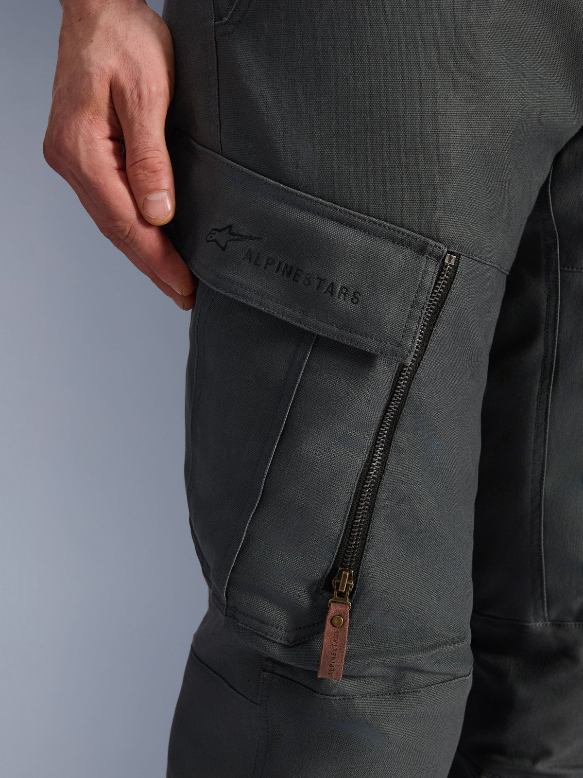 Calças Alpinestars Borrego Drystar®, Cinzento Antracite, pormenor do bolso cargo na coxa com marca bordada, material em lona encerada texturada, fecho de ventilação vertical com puxador em pele castanha