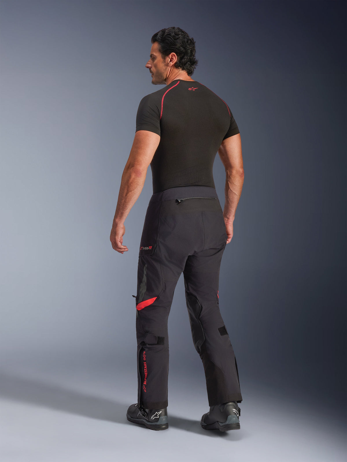 Alpinestars Halo Pro Drystar® XF Laminated Pants, Black Dark Shadow with red accents, rear view on male model, paired with a black base layer and motorcycle boots, technical adventure touring gear for all-terrain riding