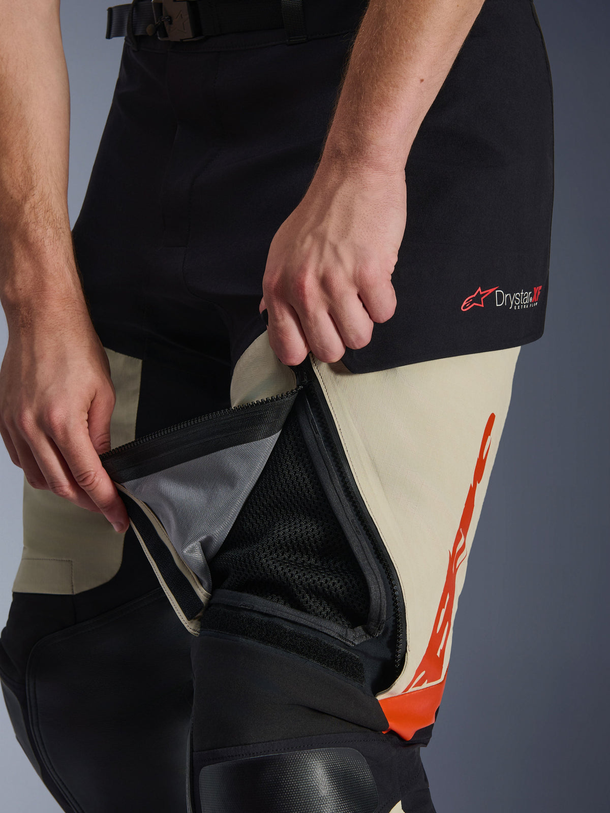 Calças Alpinestars Halo Pro Drystar® XF Laminated, Mastic Black, detalhe em grande plano da abertura de ventilação na coxa com fecho de correr aberta para revelar o painel de malha interno para circulação de ar, com logótipo Drystar XF vermelho e detalhes gráficos em cor de laranja