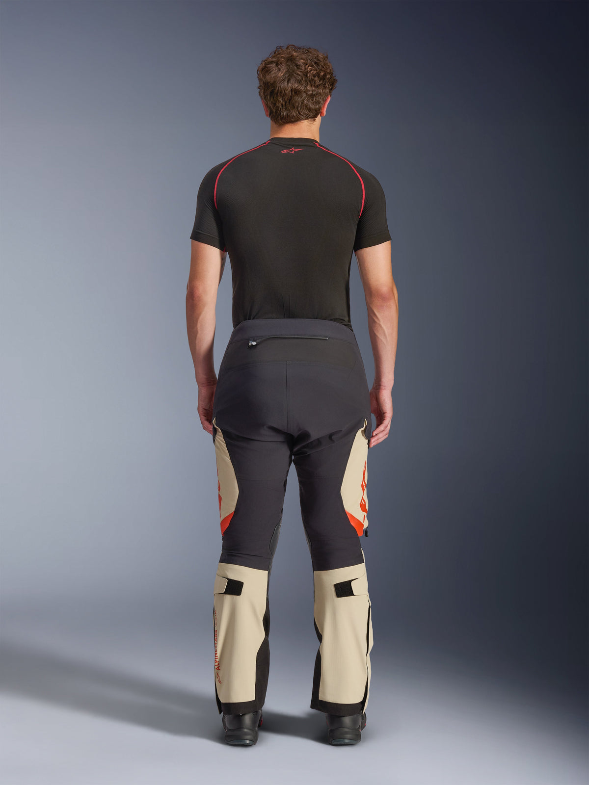 Alpinestars Halo Pro Drystar® XF Laminated Pants, Mastic Black, vista traseira num modelo, blocos de cores preto e bege com logótipos cor de laranja, calças de motociclismo de aventura e touring com construção têxtil durável e secções de panturrilha ajustáveis