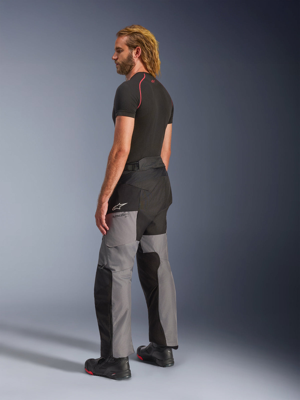 Alpinestars Andes V4 Drystar® Pants, Motorcycle Adventure Pants, Black and Dark Gray, worn with a black short-sleeved base layer and black motorcycle boots, side and back view featuring multi-panel textile design and Alpinestars branding on the thigh.
