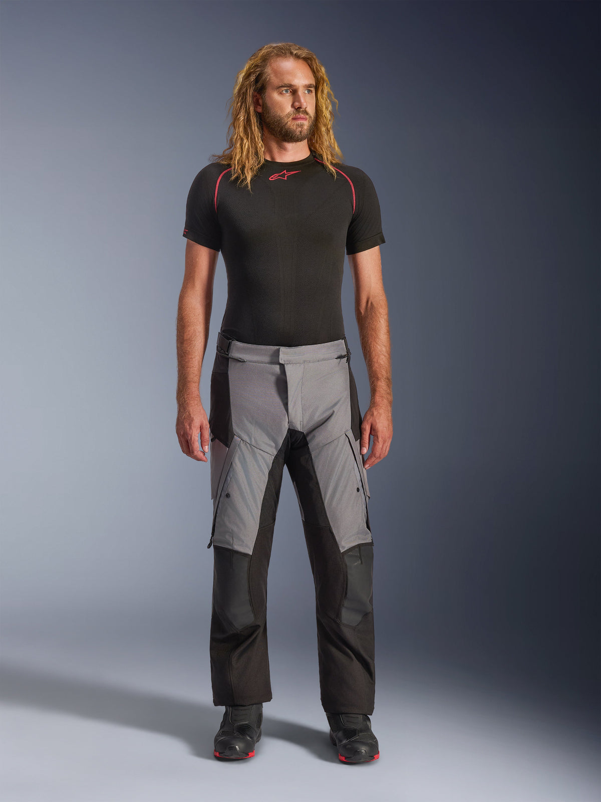 Alpinestars Andes V4 Drystar® Pants, Black and Dark Gray, adventure motorcycle pants worn by a model with a black base layer and black boots, featuring a multi-panel textile design with gray front sections and black reinforcements, designed for all-weather touring and road riding.
