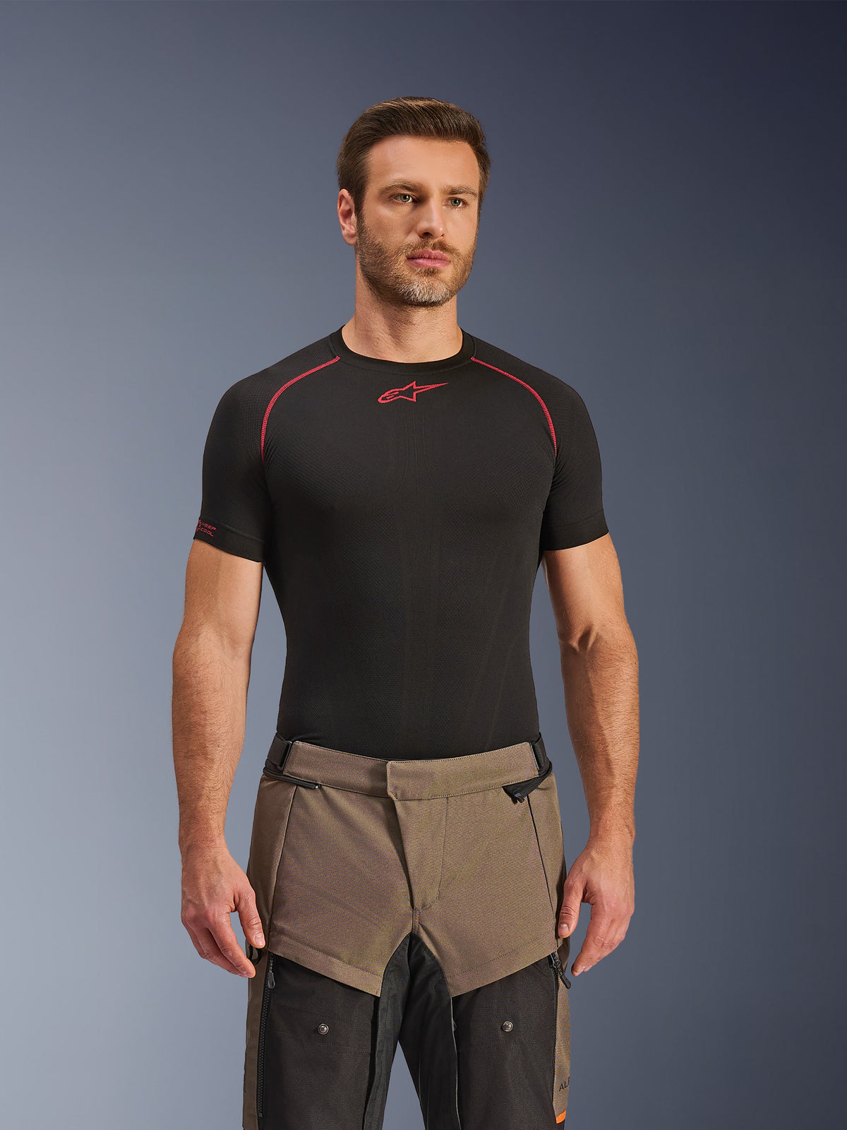 Calças Alpinestars Cusco Drystar®, calças de motociclismo de aventura Walnut Black, vestidas por um modelo com uma camisola base layer preta da Alpinestars, com um design têxtil em dois tons, castanho e preto, e painéis reforçados para touring.