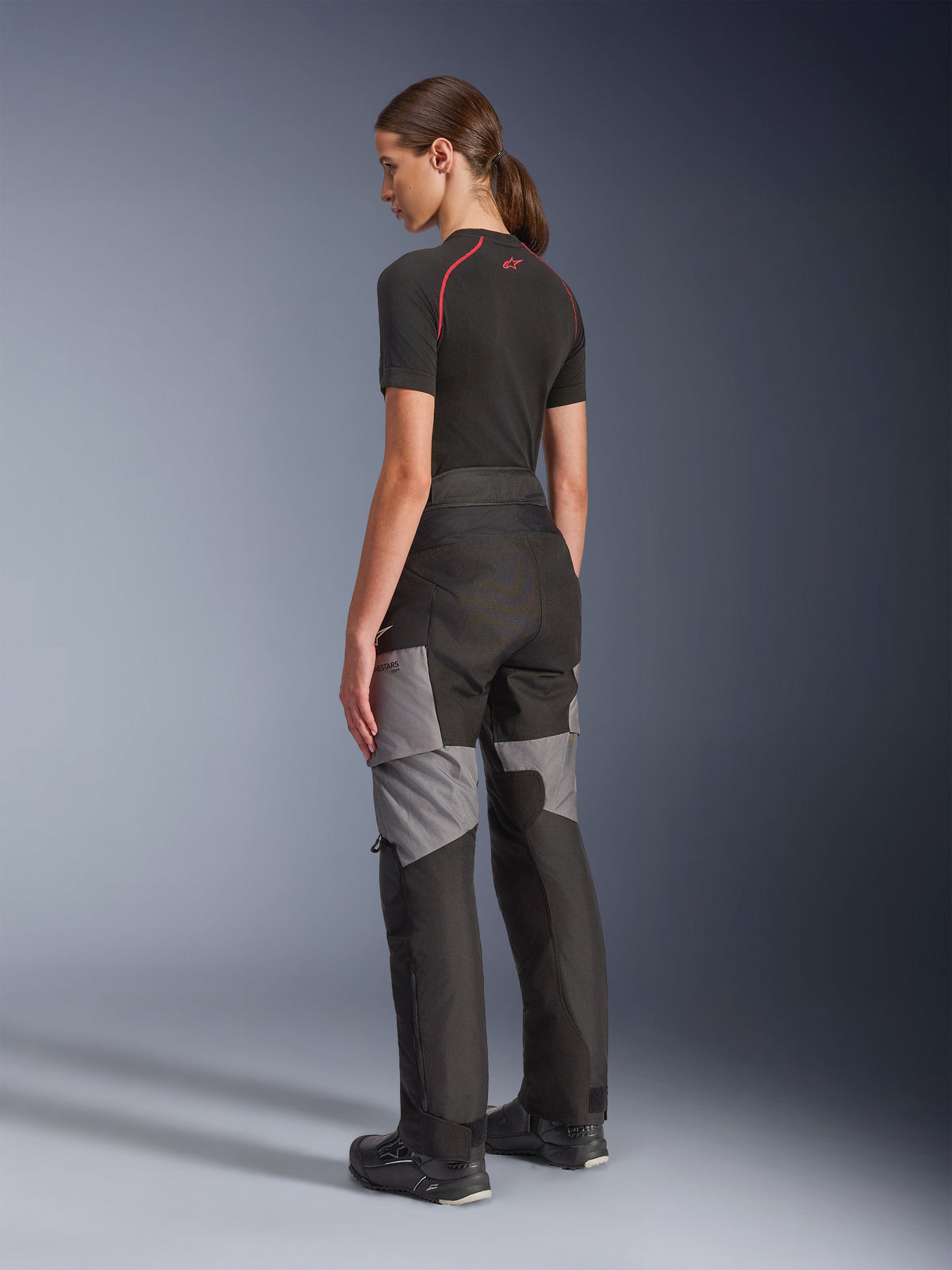 Calças Alpinestars Stella Andes V4 Drystar® para Mulher, calças de motociclismo adventure-touring pretas e cinzento escuro, vista lateral e traseira numa modelo, com construção têxtil durável, painéis de reforço cinzentos e ajuste ergonómico feminino.