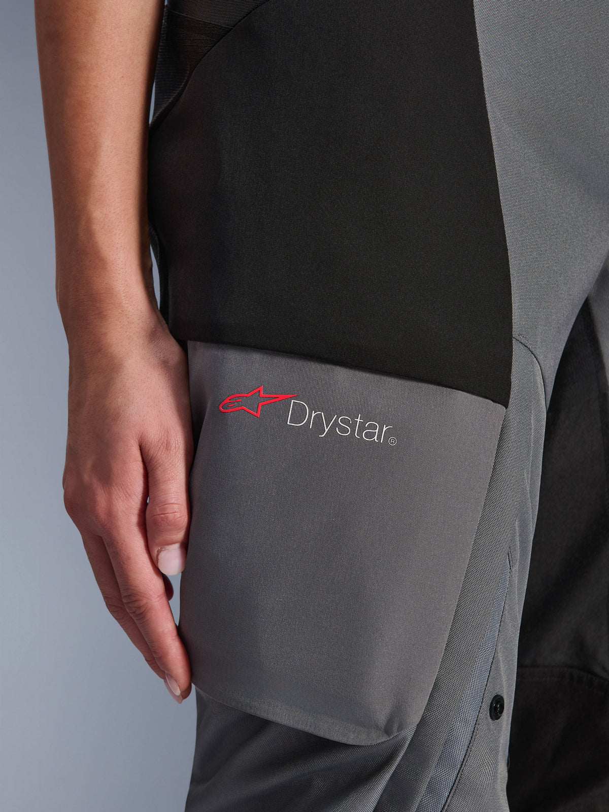 Alpinestars Stella Andes V4 Drystar® Pants, calças de aventura-touring para mulher, pretas e cinzento escuro, pormenor da zona da coxa mostrando o logótipo Drystar e a estrela Alpinestars vermelha em painéis têxteis reforçados